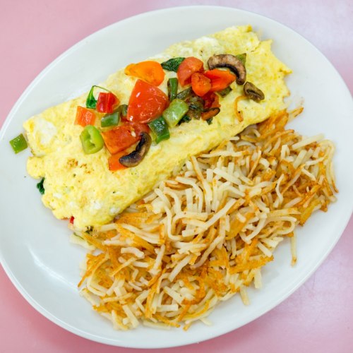 A fluffy omelette topped with diced vegetables, served alongside crispy hash browns on a white plate.