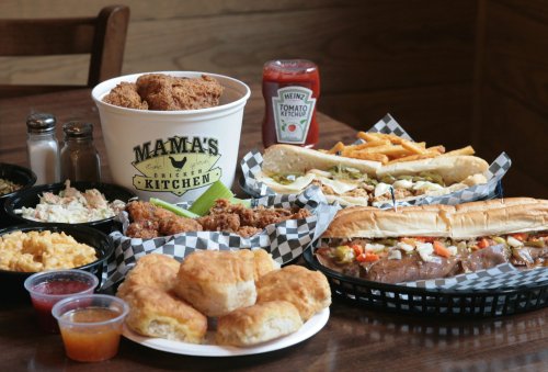 A spread of comfort food including fried chicken, sandwiches, fries, biscuits, and condiments on a wooden table.