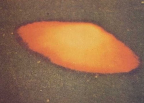 An irregular orange shape on a dark surface, resembling a small puddle or stain.