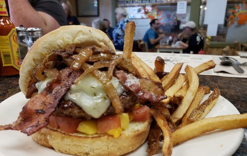 A hearty burger topped with bacon, cheese, and onions, served with a side of crispy fries on a plate.