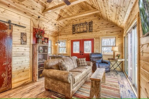 Cozy wooden cabin interior featuring a sofa, coffee table, and red doors, with natural light and rustic decor.