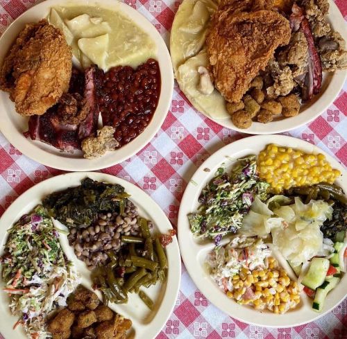 A spread of Southern dishes including fried chicken, collard greens, corn, beans, and various sides on plates.