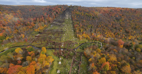Aerial view of a rusted, abandoned structure amidst vibrant autumn foliage on rolling hills.