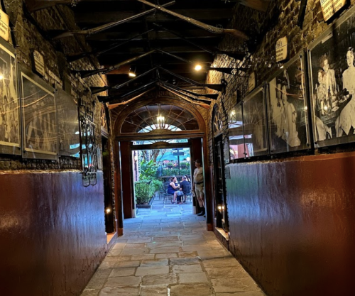 A dimly lit corridor with historical photos on the walls, leading to an outdoor seating area.