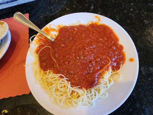 A plate of spaghetti topped with a rich red meat sauce, served with a spoon on a dark countertop.