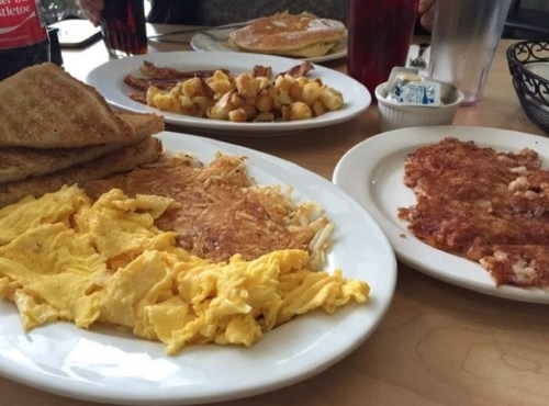 A breakfast spread featuring scrambled eggs, hash browns, toast, and a side of crispy bacon on a table.