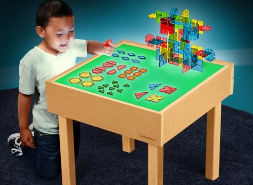 A child plays with colorful geometric shapes on a light-up activity table, exploring creativity and design.