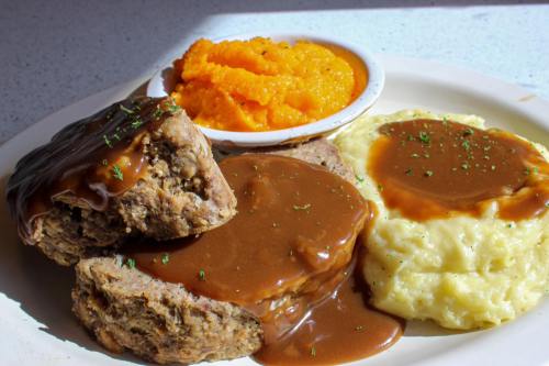 A plate of meatloaf with gravy, creamy mashed potatoes, and a side of sweet potato mash.