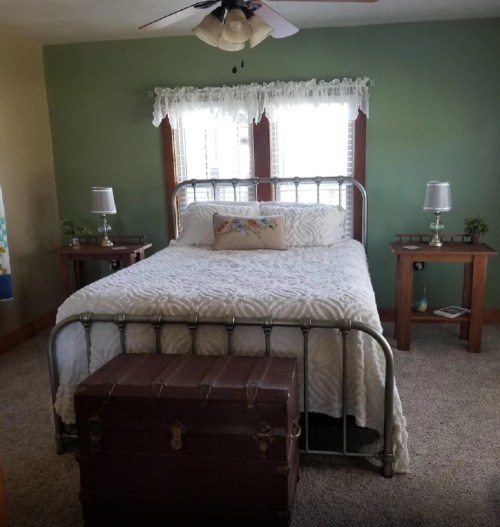 Cozy bedroom featuring a metal bed, decorative pillows, wooden nightstands, and a vintage trunk at the foot of the bed.