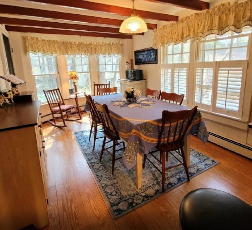 A cozy dining room with a wooden table, chairs, and large windows, featuring warm lighting and decorative curtains.
