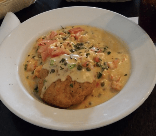 A bowl of shrimp and tomato stew served over a biscuit, topped with creamy sauce and herbs.