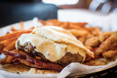 A close-up of a burger topped with cheese and an egg, served with crispy fries and fried pickles in a basket.