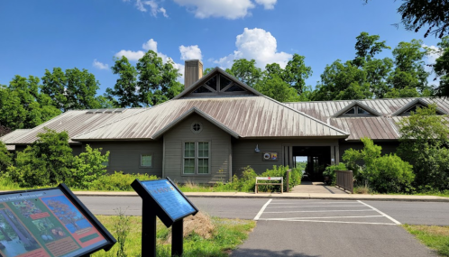 A modern building with a sloped roof surrounded by greenery, featuring informational signs in the foreground.