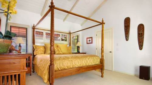 A cozy bedroom featuring a four-poster bed with golden bedding, wooden furniture, and decorative masks on the walls.
