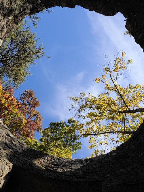 View looking up from a stone well, framed by colorful autumn leaves against a blue sky.