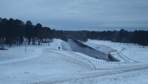 A snowy landscape with a river winding through trees, under a cloudy sky.