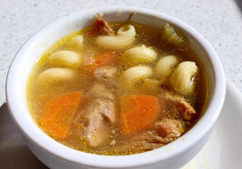 A bowl of hearty soup with noodles, carrots, and pieces of meat in a savory broth.