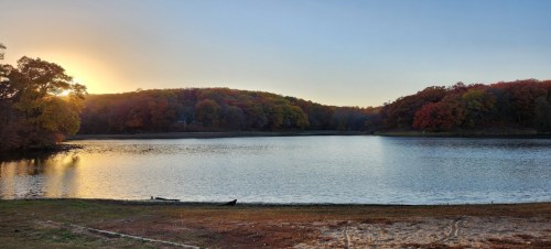 A serene lake at sunset, surrounded by colorful autumn trees and a calm water surface reflecting the sky.