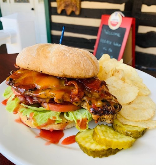 A delicious burger with bacon, cheese, lettuce, and tomato, served with chips and pickles on the side.