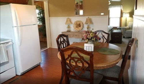 A cozy kitchen with a round wooden table, chairs, a white refrigerator, and a decorative side table with flowers.