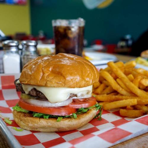 A juicy hamburger with lettuce, tomato, and cheese, served with crispy fries and a glass of cola on a tray.