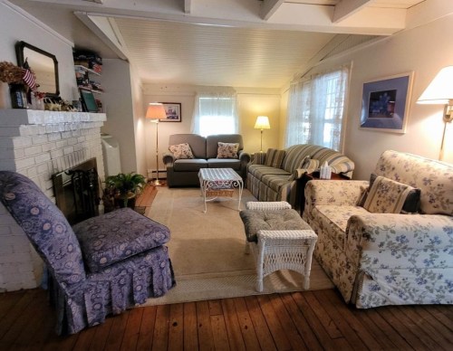 Cozy living room with floral sofas, a coffee table, and a fireplace, featuring warm lighting and wooden floors.