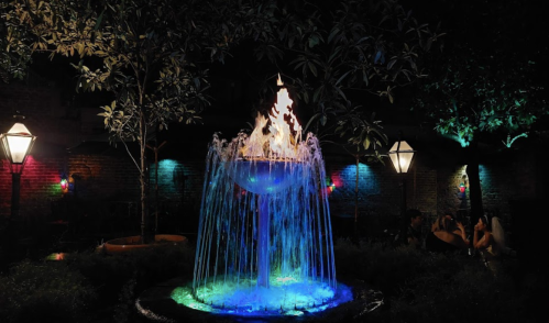 A vibrant fountain with colorful lights at night, surrounded by trees and illuminated lanterns.