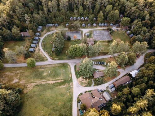 Aerial view of a wooded area with cabins, tennis courts, and winding roads surrounded by trees.