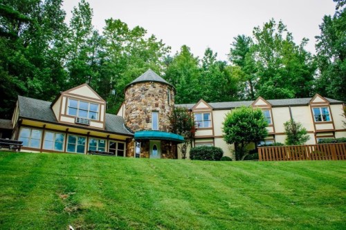 A unique stone and wood building with a tower, surrounded by green grass and trees.