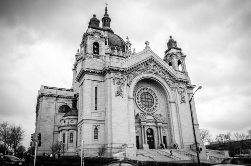 A grand, historic church with intricate architecture, featuring a large circular window and domed towers, set against a cloudy sky.