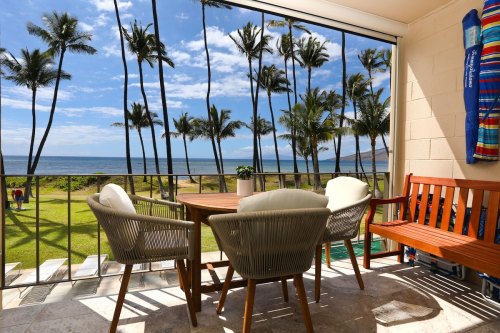 A scenic view from a balcony featuring a table and chairs, with palm trees and ocean in the background.