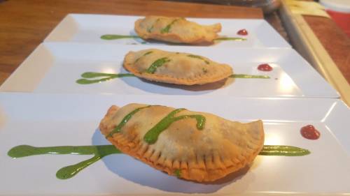 Three golden-brown empanadas drizzled with green sauce and a small dollop of red sauce on a white plate.