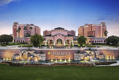 Exterior view of Caribe Royale Orlando, featuring a large fountain and palm trees against a sunset sky.