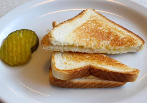 Grilled cheese sandwich cut in half, served with two slices of pickles on a white plate.