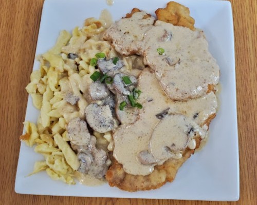 A plate of breaded meat topped with creamy mushroom sauce, served alongside egg noodles.