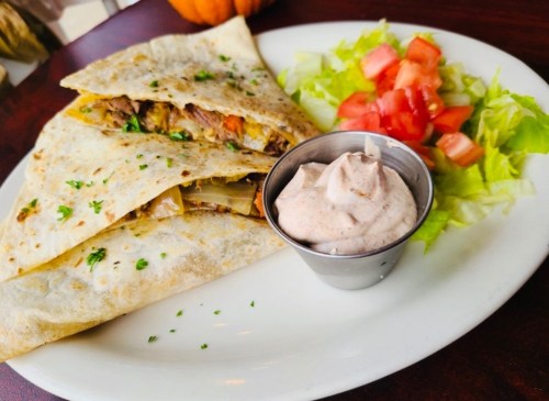 A plate featuring a folded tortilla filled with meat and vegetables, accompanied by a side salad and dipping sauce.