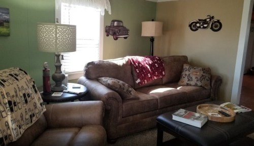 Cozy living room with a brown sofa, lamp, motorcycle decor, and a coffee table with books and a tray.