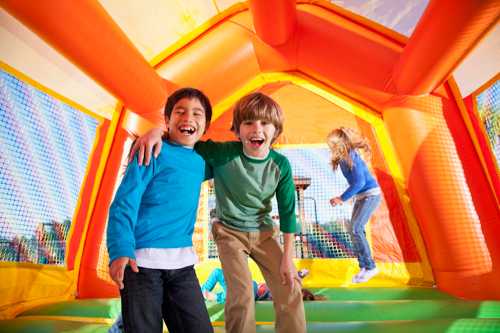 Two smiling boys pose together inside a colorful bounce house, with other children playing in the background.