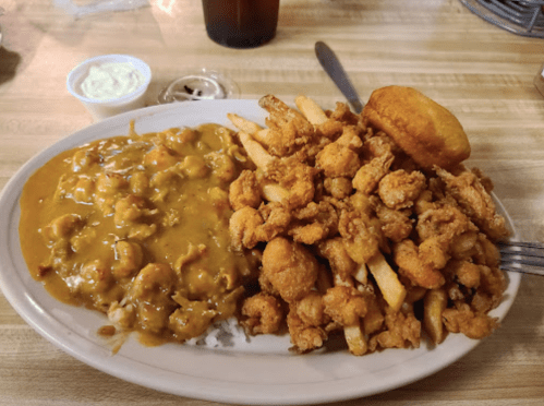 A plate of fried shrimp with French fries, a biscuit, and a side of gravy.