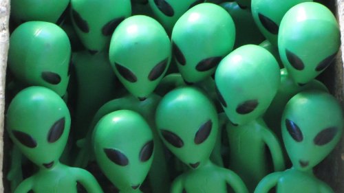 A group of small green alien figurines with large black eyes, packed closely together in a box.