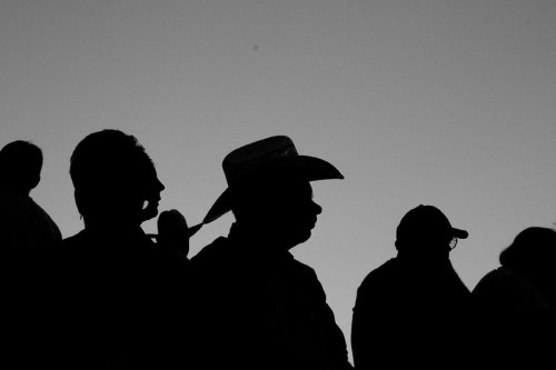 Silhouettes of people, including one wearing a cowboy hat, against a light sky background.