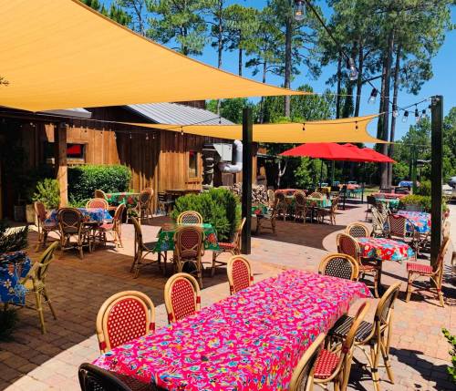 Outdoor dining area with colorful tables and chairs, shaded by yellow canopies, surrounded by trees and greenery.