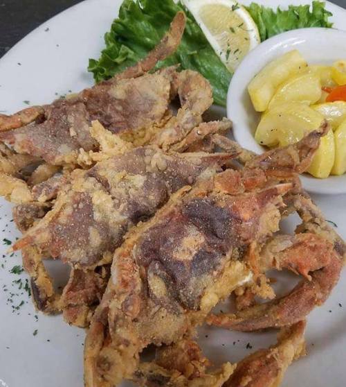 A plate of fried soft-shell crabs garnished with lettuce and a lemon wedge, served with a side of mixed vegetables.