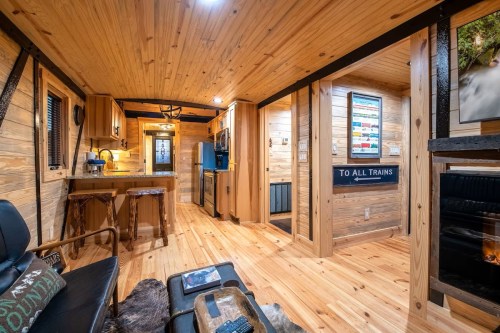 Cozy interior of a tiny home with wooden walls, a kitchen area, and a living space featuring rustic decor.