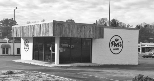 A black and white image of a modern building with a wooden overhang, featuring a sign that reads "Poet's South."