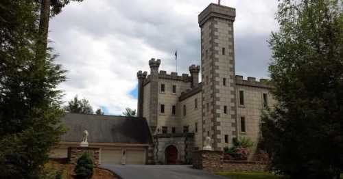 A large stone castle with a tall tower, surrounded by trees and a driveway leading to the entrance.