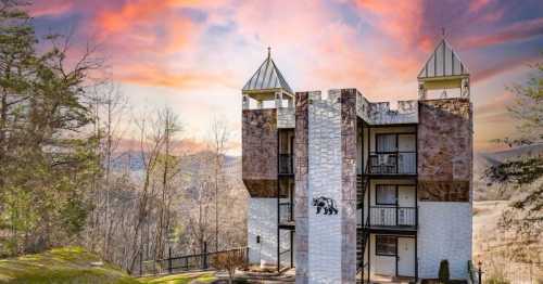 A unique castle-like building with towers, surrounded by trees and a colorful sunset sky.