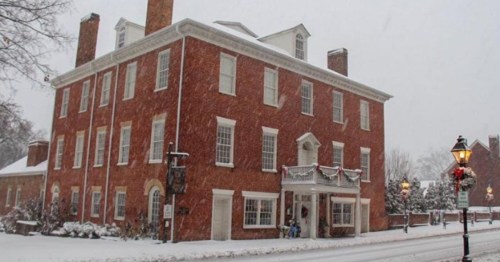 A historic brick building covered in snow, with festive decorations and a lamppost in a wintery street scene.