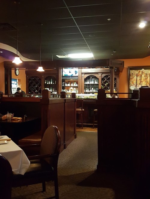 Interior of a restaurant featuring wooden decor, a bar area, and dim lighting, with tables set for dining.