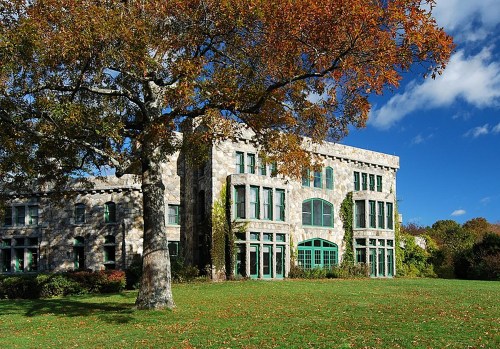 A stone building with large windows surrounded by green grass and autumn trees under a blue sky.